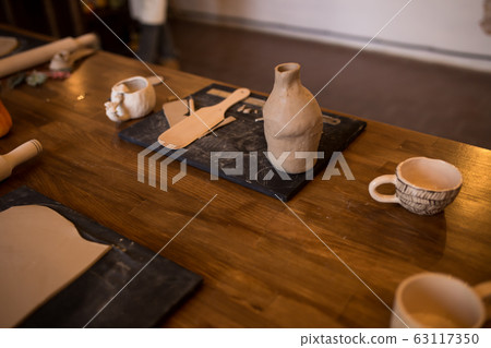A master class in modeling a clay jug. Table with clay and a tool for creativity. A master class in modeling a clay jug. Table with clay and a tool for creativity. 63117350
