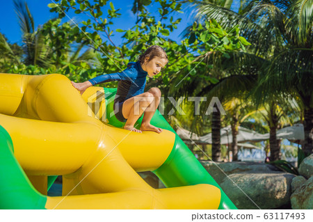 Cute boy runs an inflatable obstacle course in the pool Cute boy runs an inflatable obstacle course in the pool 63117493