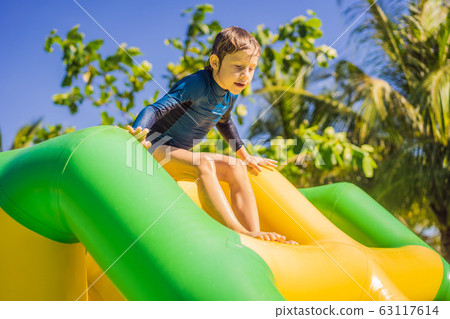 Cute boy runs an inflatable obstacle course in the pool 63117614