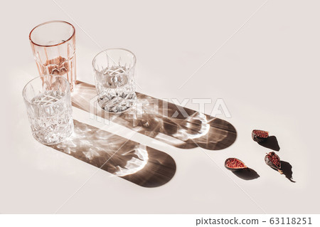 Summer still life scene. Glittering glasses of water or cocktails and cut figs fruit on pink table background in sunlight. Long harsh shadows. High angle. Refreshment, vacation concept. 63118251
