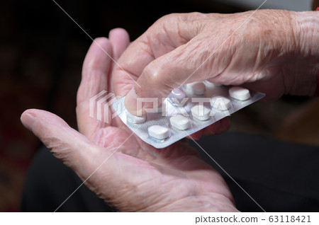 Hands of an old woman close-up. The old woman unpacks the tablets before use 63118421