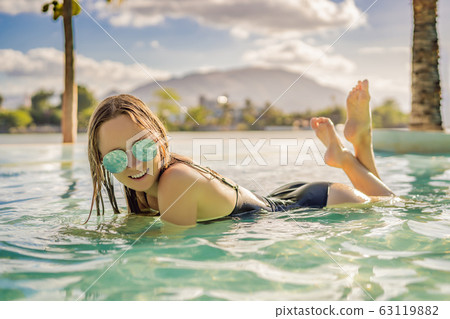 Luxury resort swimming pool. Beautiful woman tourist relaxing in holiday retreat on summer travel Luxury resort swimming pool. Beautiful woman tourist relaxing in holiday retreat on summer travel 63119882