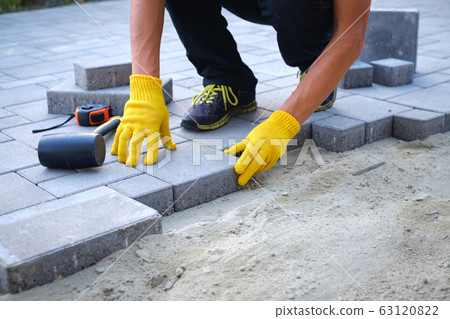 The master in yellow gloves lays paving stones The master in yellow gloves lays paving stones 63120822