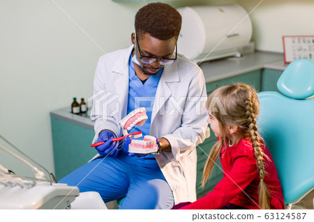 Young beautiful girl in dental office. African children's dentist examines teeth to a child. 63124587