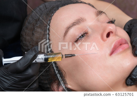 hand with syringe at the patient cheek 63125701