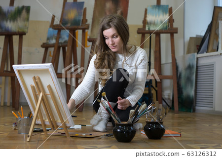 Woman artist sits on the floor among easels with Woman artist sits on the floor among easels with 63126312
