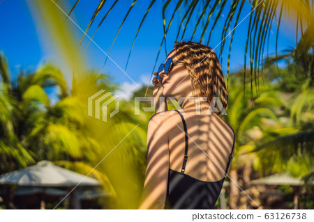Young woman with the shadow of the palm leaf on her back. Relaxing on the seaside 63126738
