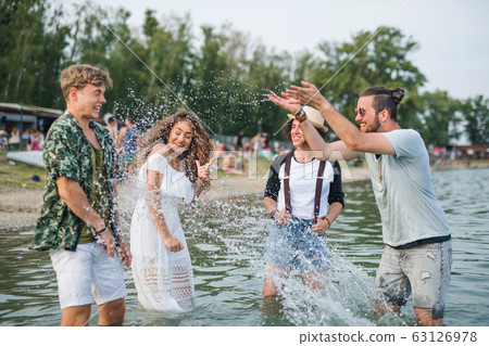 Group of young friends at summer festival, standing in lake. 63126978