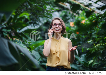 Young woman with smartpone standing in botanical garden. Copy space. Young woman with smartpone standing in botanical garden. Copy space. 63127753