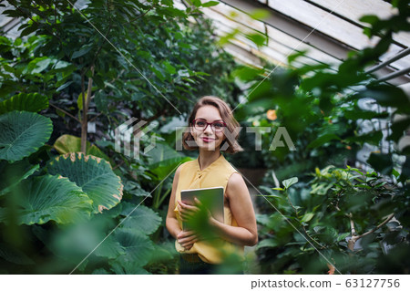 Young woman with tablet standing in botanical garden. Copy space. 63127756
