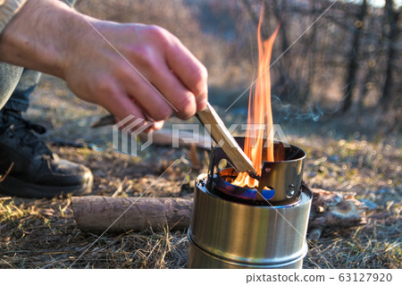 closeup man hands sets fire with straws a in a portable wood burner in mountains 63127920