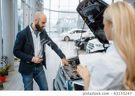 Man and saleslady choosing auto in car dealership 63133247