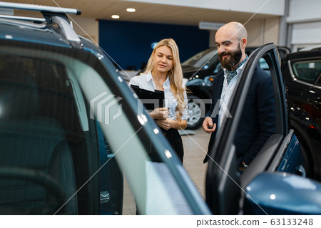 Smiling man and saleswoman in car dealership 63133248