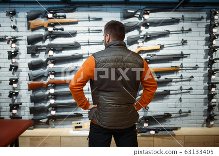 Man at showcase with rifles, back view, gun shop Man at showcase with rifles, back view, gun shop 63133405