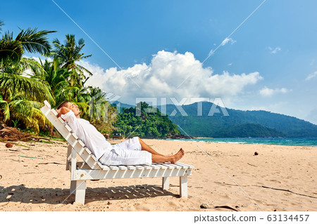 Man in white relaxing in sun bed on beach Man in white relaxing in sun bed on beach 63134457