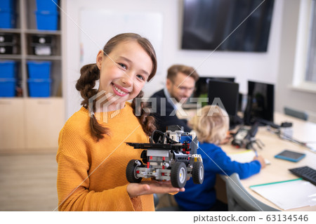 Girl holding buildable car and smiling, teacher and boy in background 63134546