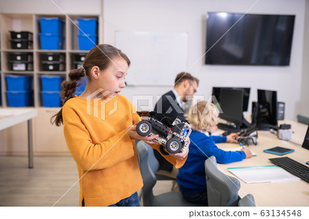 Girl holding buildable car, teacher and boy in background 63134548