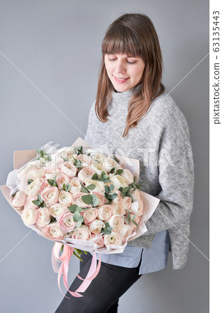 Persian buttercup in womans hands. Bunch pale pink ranunculus flowers with green eucalyptus. The work of the florist at a flower shop Persian buttercup in womans hands. Bunch pale pink ranunculus flowers with green eucalyptus. The work of the florist at a flower shop 63135443