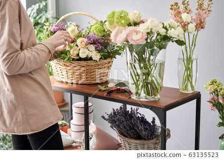 Floral shop concept . Florist woman creates flower arrangement in a wicker basket. Beautiful bouquet of mixed flowers. Handsome fresh bunch. Flowers delivery. 63135523