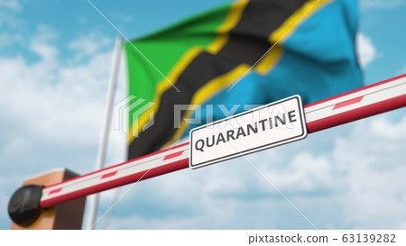 Closing boom barrier with QUARANTINE sign against the Tanzanian flag. Restricted border crossing or infection related isolation in Tanzania Closing boom barrier with QUARANTINE sign against the Tanzanian flag. Restricted border crossing or infection related isolation in Tanzania 63139282