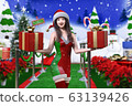 在雪域中，一個年輕的日本人在一個穿著聖誕服裝的雪人面前笑著，雙手捧著一盒禮物 63139426