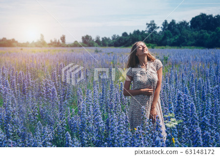 a girl in a loose dress with her hair down walks through a flower meadow. A woman enjoys life among purple flowers . The concept of summer, warmth, freedom, and the scent of spring a girl in a loose dress with her hair down walks through a flower meadow. A woman enjoys life among purple flowers . The concept of summer, warmth, freedom, and the scent of spring 63148172