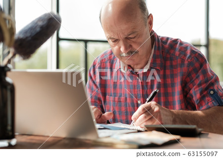 Mature hispanic man sitting at his desk and taking notes Mature hispanic man sitting at his desk and taking notes 63155097