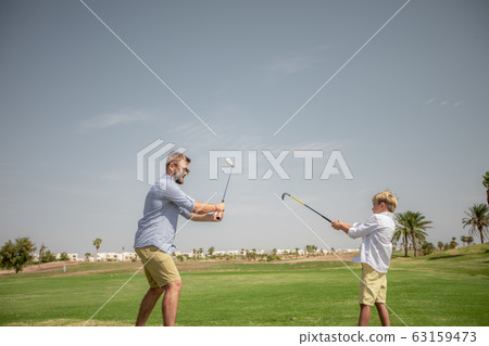 Father has fun and teaches his son to play golf on the green grass 63159473