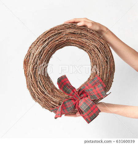 Woman's hands hold round wreath from dry twigs with bow. 63160039