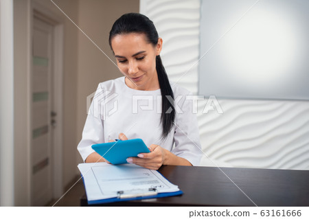 Receptionist holding little tablet while making appointment Receptionist holding little tablet while making appointment 63161666