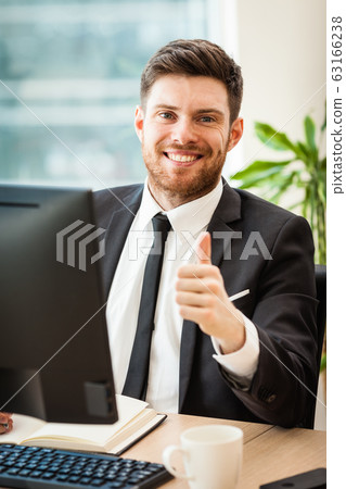 Young businessman in office sitting at his desk Young businessman in office sitting at his desk 63166238