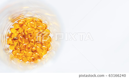 Orange pills inside glass jar. Top view on medicine capsules. White background with copy space. Orange pills inside glass jar. Top view on medicine capsules. White background with copy space. 63166240
