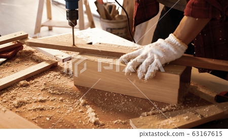 Carpenter using drill to screwing pieces of board at site. 63167615