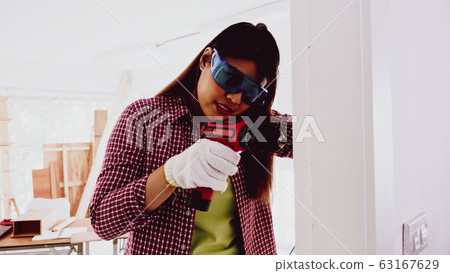 Female carpenter using drill to screwing wall at site. 63167629