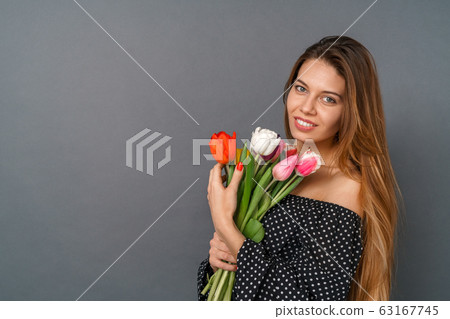 Young woman casual studio isolated on gray with bouquet of tulips looking camera tender Young woman casual studio isolated on gray with bouquet of tulips looking camera tender 63167745