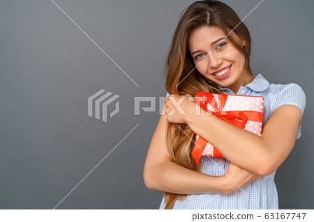 Young woman in dress studio isolated on gray hugging gift box Young woman in dress studio isolated on gray hugging gift box 63167747
