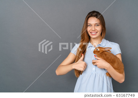 Young woman in dress studio isolated on gray with little bunny thumb up Young woman in dress studio isolated on gray with little bunny thumb up 63167749