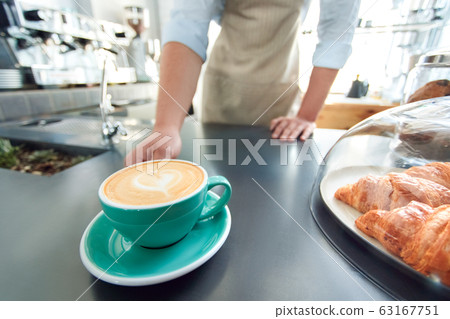 Young adult barista working in cafeteria, standing near cup of coffee Young adult barista working in cafeteria, standing near cup of coffee 63167751
