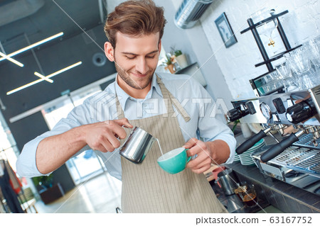 Coffee Passion. Young barista at coffee shop pouring steamed milk into cup with espresso making latte art smiling joyful Coffee Passion. Young barista at coffee shop pouring steamed milk into cup with espresso making latte art smiling joyful 63167752