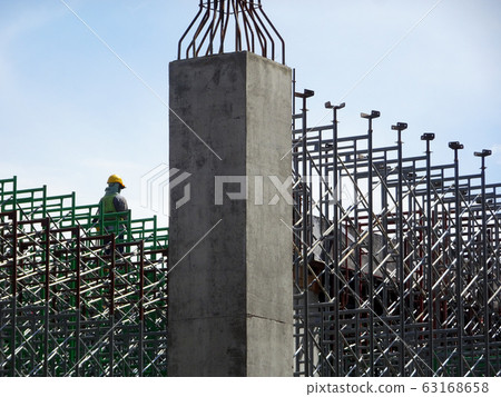 Construction workers wearing safety gear and safety harness while installing scaffolding at a high level in the construction site. Construction workers wearing safety gear and safety harness while installing scaffolding at a high level in the construction site. 63168658