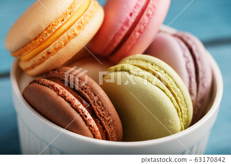 Multicolored French macaroni cookies in a white plate, on a blue wooden background. Free space, top View. Multicolored French macaroni cookies in a white plate, on a blue wooden background. Free space, top View. 63170842