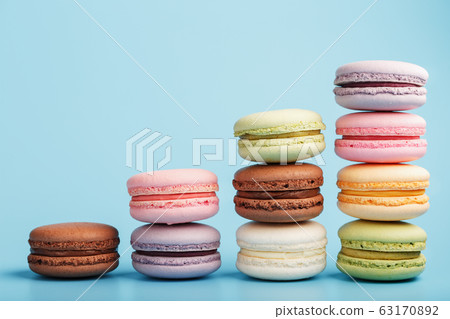 Multicolored French macaroni macaroni cookies are arranged in a pyramid on a blue background. Multicolored French macaroni macaroni cookies are arranged in a pyramid on a blue background. 63170892