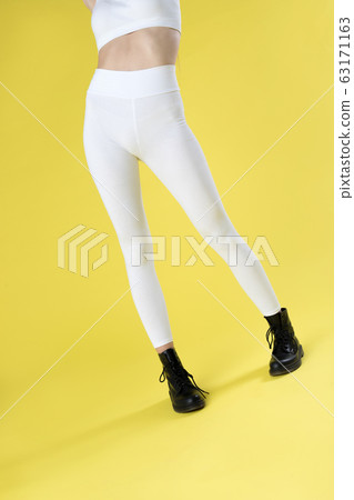Young woman in white blank leggings and a crop top on a yellow background. Mock-up. Young woman in white blank leggings and a crop top on a yellow background. Mock-up. 63171163