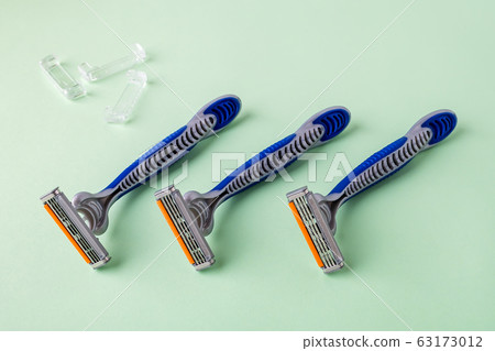 Three new disposable shaving razors with triple blade lie in a row on a pastel green background. 63173012