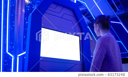 Woman looking at blank white display kiosk at exhibition - white screen concept Woman looking at blank white display kiosk at exhibition - white screen concept 63173248