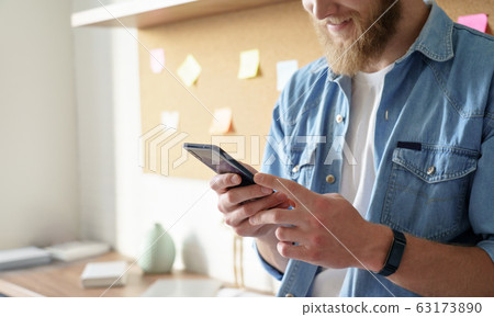Close up view of young man standing at home office using smart phone mobile app. 63173890
