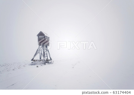 Deer stand, wooden hunters high seat hide on snow covered field, winter foggy day 63174404