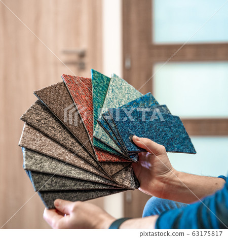 the man chooses the color of the new carpet according to the samples in the flooring shop 63175817