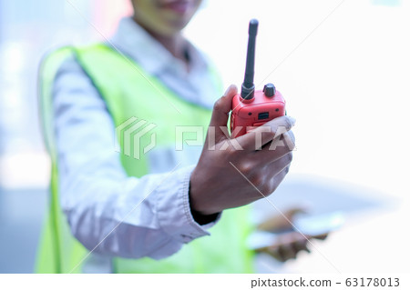 Hand of technician worker woman hold and shows red walky-talky in cargo container area 63178013