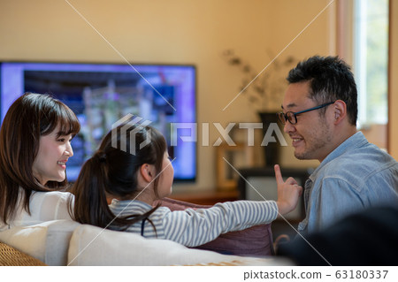 Image of three parents and children (father, mother, daughter) watching TV on the sofa Image of three parents and children (father, mother, daughter) watching TV on the sofa 63180337